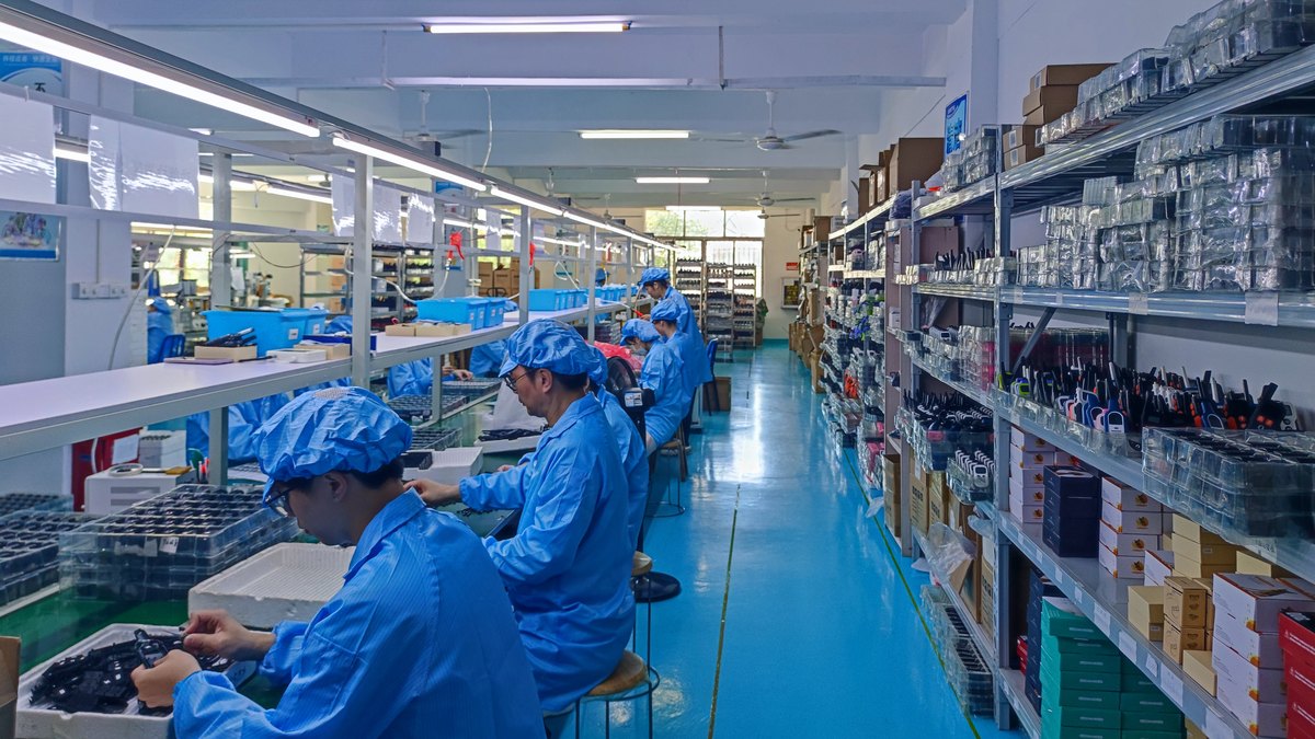 Electronics production line in operation, with assembly stations along the bench and component stores on the racking alongside